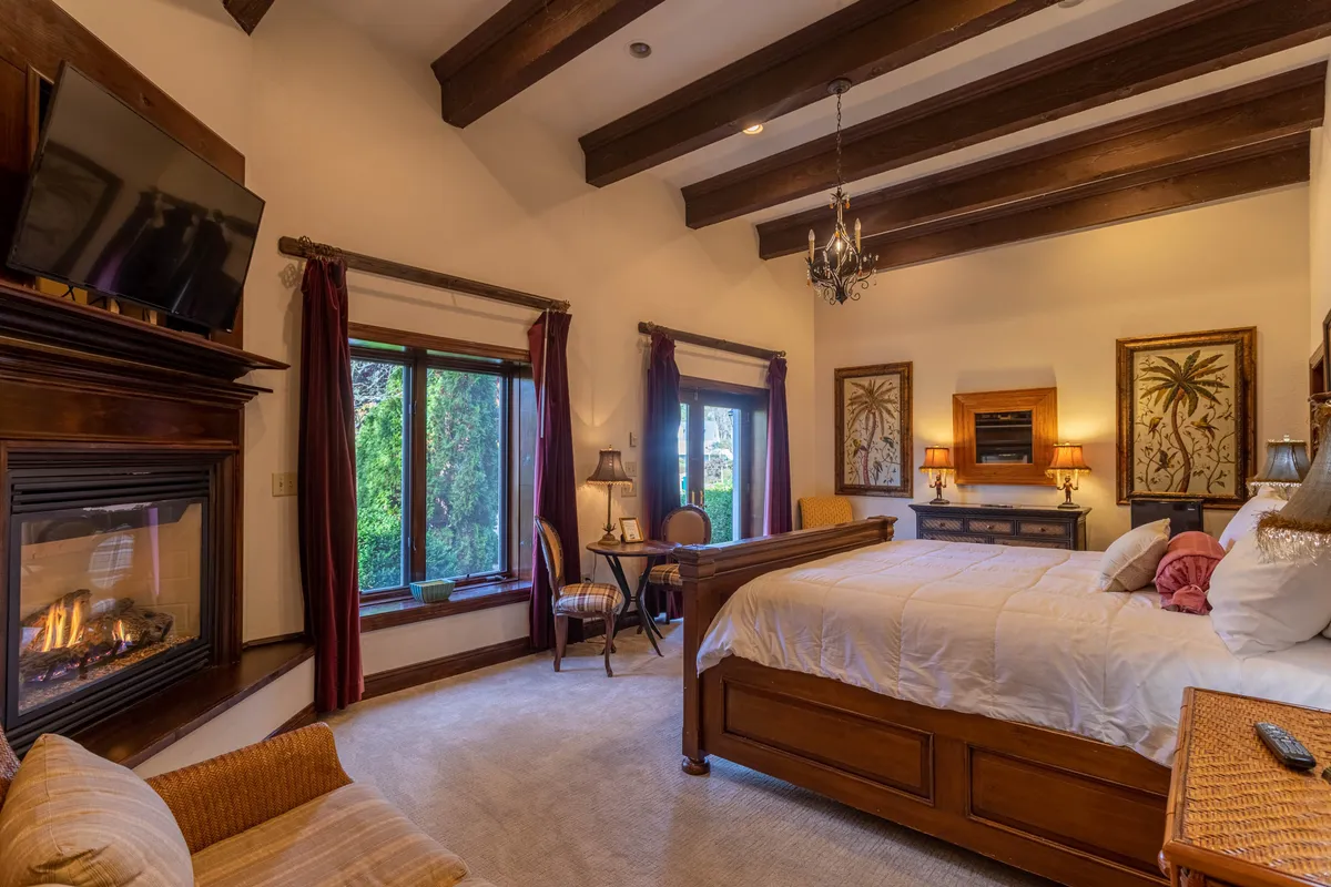 A luxurious suite featuring a king-sized bed positioned beside a warm fireplace, with large windows looking out onto the scenery and elegant decorative artwork adding a touch of sophistication. The room exudes comfort and is perfect for relaxing after a day spent outdoors, especially during ski season or colder months.