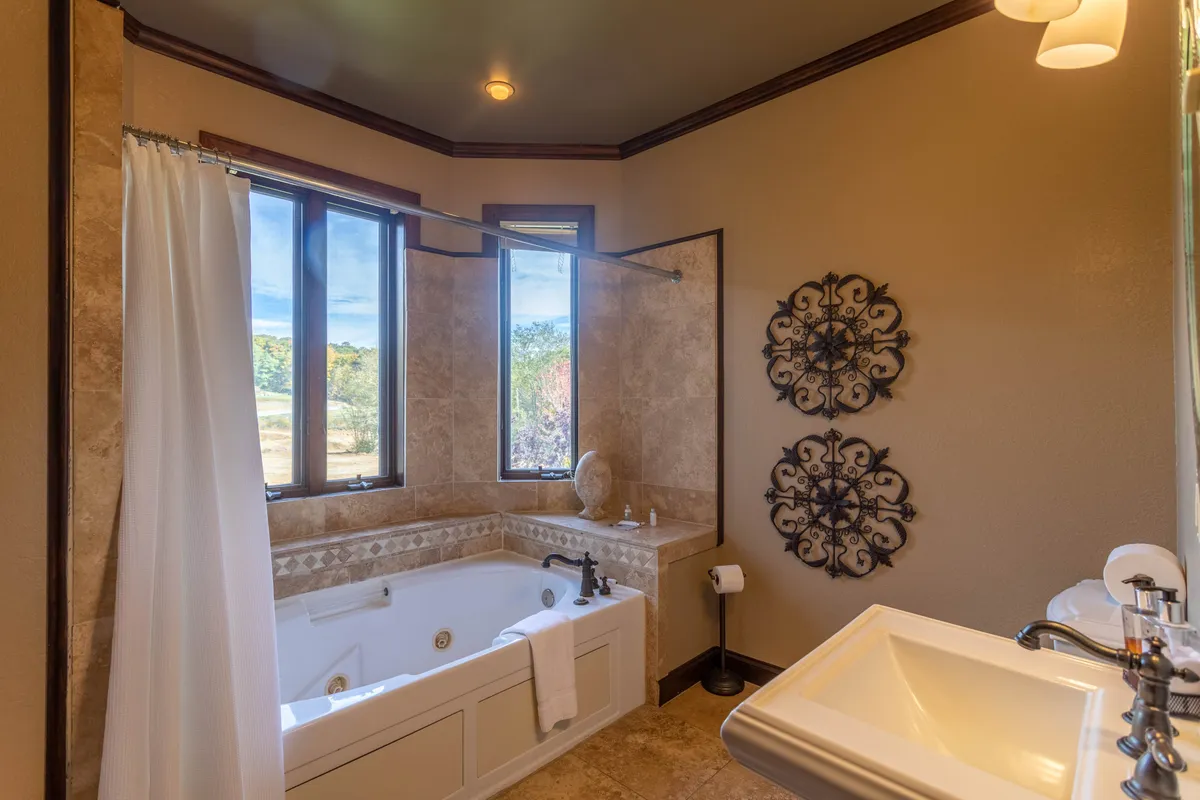 This suite bathroom includes a spacious soaking bathtub positioned near windows, allowing for relaxation while enjoying scenic views. The decor is serene and luxurious, with thoughtful touches like decorative wall art and ample natural light.