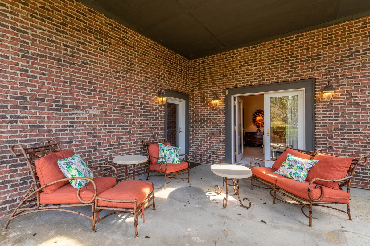 A rustic brick-walled patio area featuring comfortable seating with decorative pillows, open doors leading inside, and warm light fixtures. The setting is both welcoming and versatile—ideal for morning sunrises, afternoon gatherings, or starlit evenings.