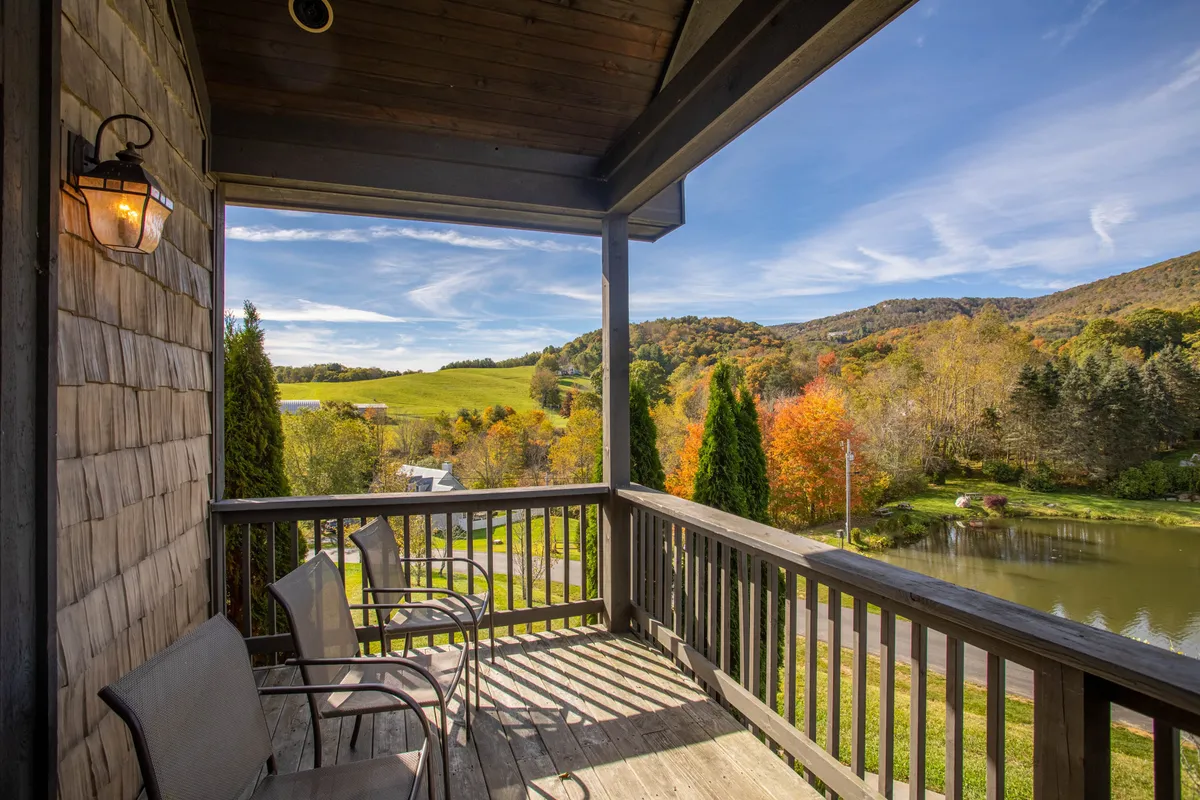 A tranquil balcony overlooking a serene pond, surrounded by autumn foliage and distant mountains. The comfortable seating area invites relaxation while enjoying breathtaking estate views.