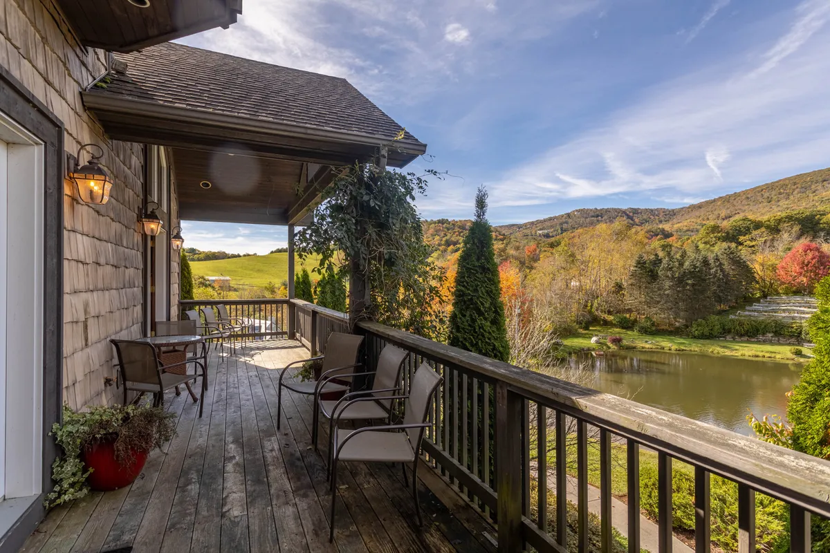An expansive deck furnished with comfortable chairs, overlooking a stunning waterfront with a mountain backdrop and lush greenery. The setting is serene, ideal for morning coffee, outdoor dining, or simply savoring the views of the surrounding nature.