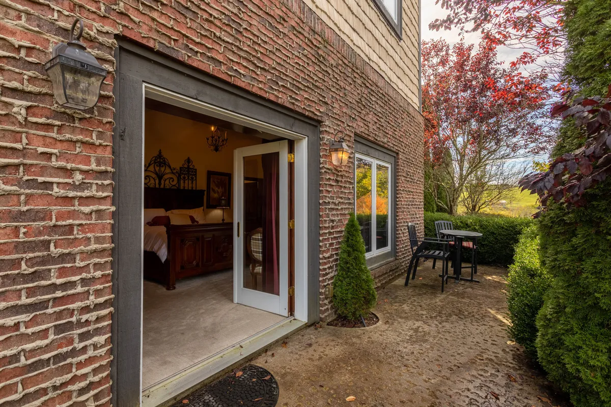 A tranquil patio scene featuring French doors opening onto an outdoor seating area surrounded by tasteful landscaping. The setup invites guests to unwind outdoors, enjoy morning coffee, or relax with a glass of wine while taking in the serene surroundings.