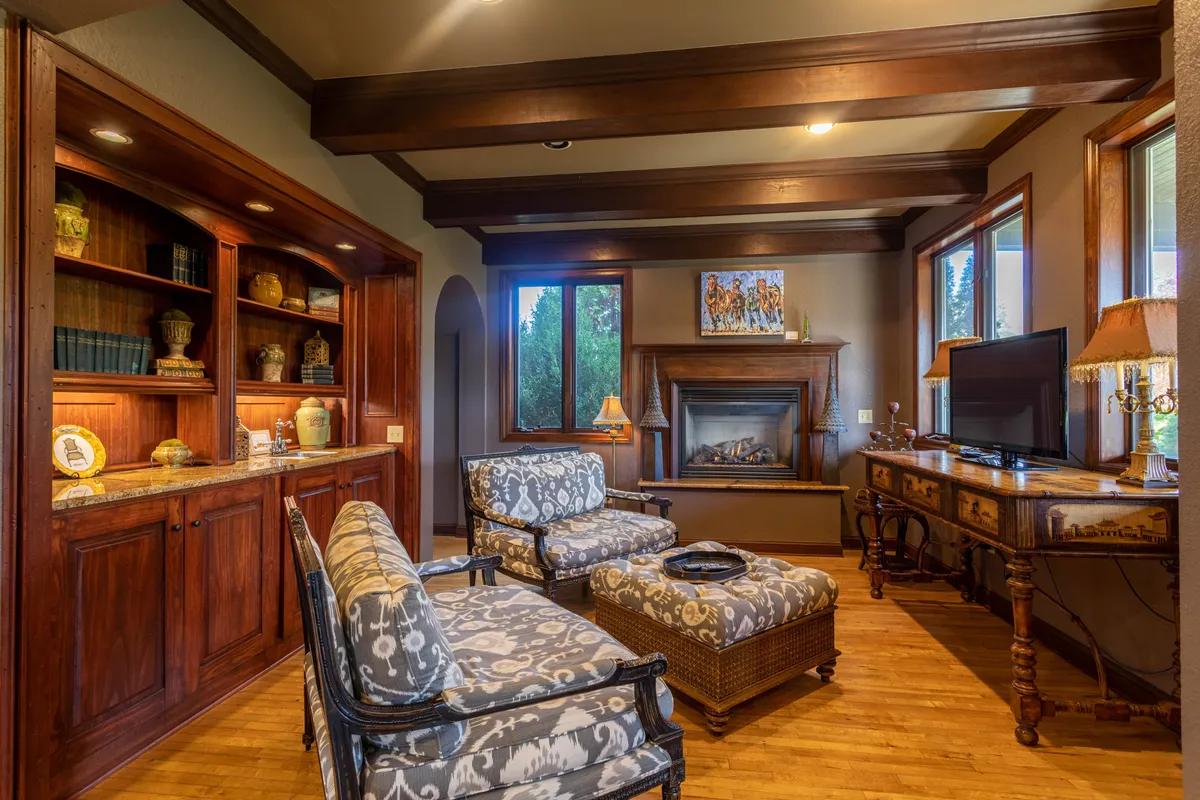 A welcoming great room featuring a gas fireplace at its center, flanked by built-in bookshelves, plush armchairs, a coffee table, and tastefully arranged decorative items. The ambiance is cozy, with soft lighting and ample space for guests to gather and socialize. The overall mood is warm and inviting, perfectly suited to relaxed evenings or lively group activities.