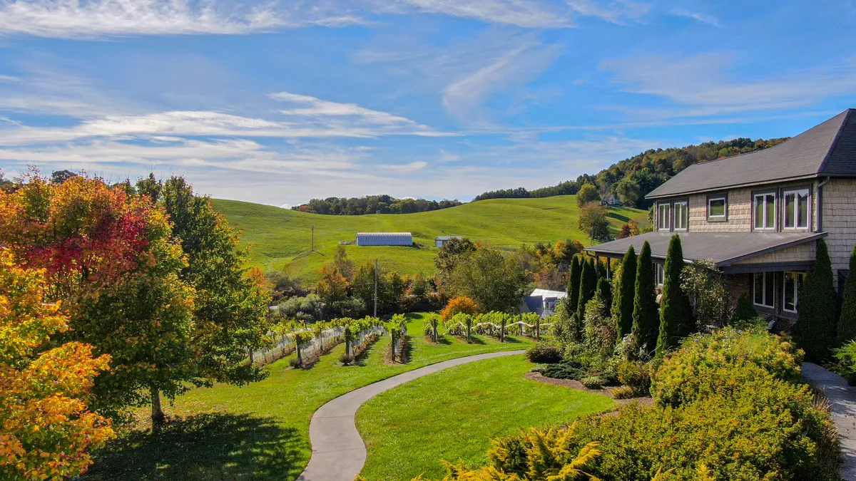A sweeping exterior shot showcasing vibrant vineyard rows set against rolling hills, with a charming house nestled among the landscape. The scene is bathed in soft sunset light, highlighting the tranquility and beauty of wine country.
